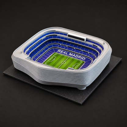 Model stadionu Santiago Bernabéu bez střechy na černé podložce, pohled na modré tribuny a zelené hřiště.