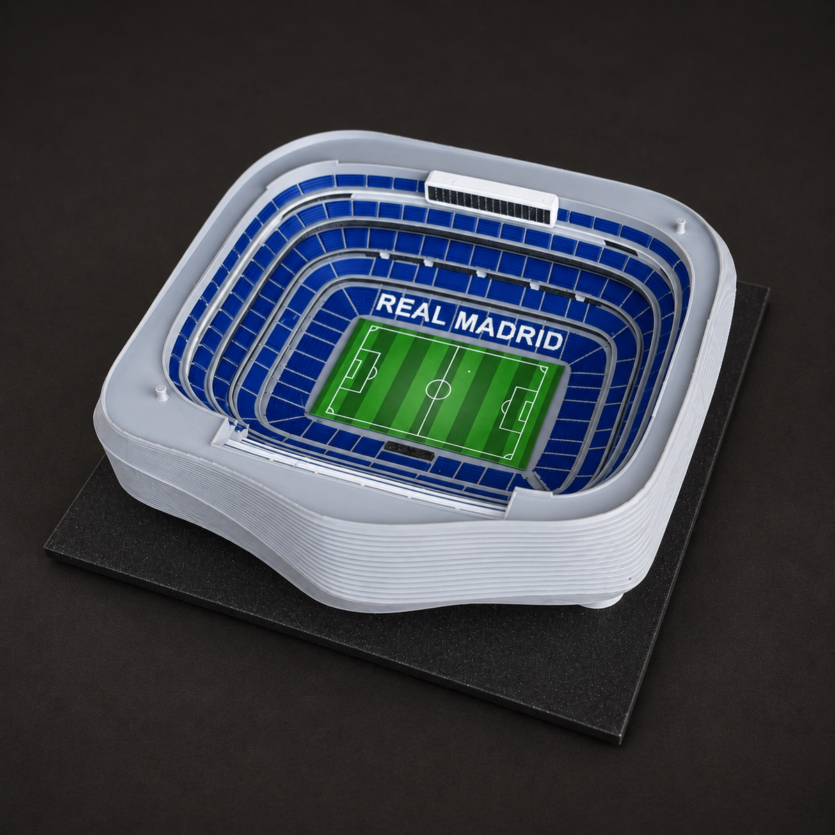Detail interiéru modelu Santiago Bernabéu s modrými tribunami, nápisem REAL MADRID a zeleným hřištěm.