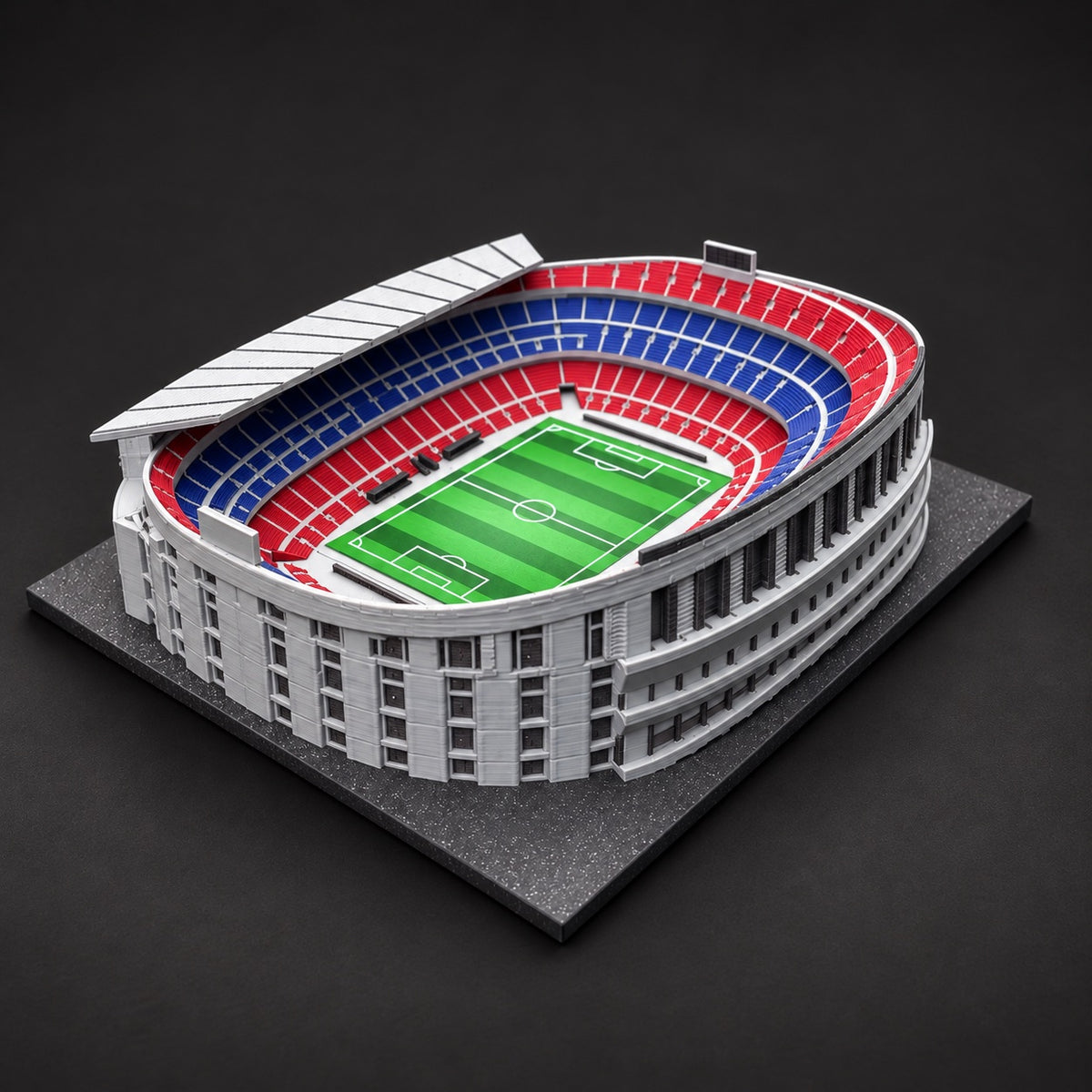 Barevný model původního stadionu Camp Nou s červenými a modrými tribunami na černé podložce.