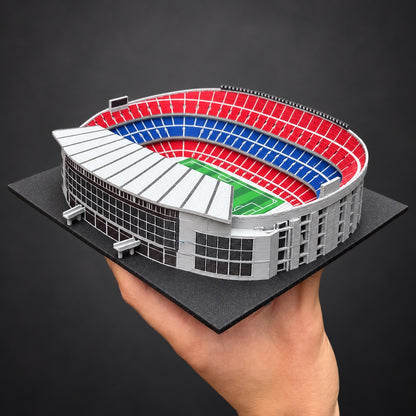 Skutečný model Camp Nou držený v ruce pro představu o velikosti. Studiově upravené pozadí.